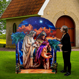 A woman stands next to a large, colorful nativity scene depicting three figures in robes and headdresses, with a castle and starry sky in the background.