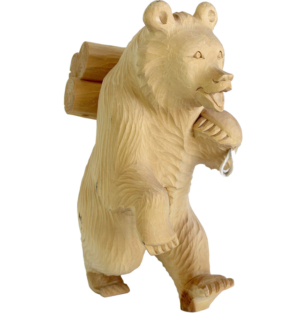 A wooden bear sculpture with a backpack on its back, standing upright and carrying a large log.