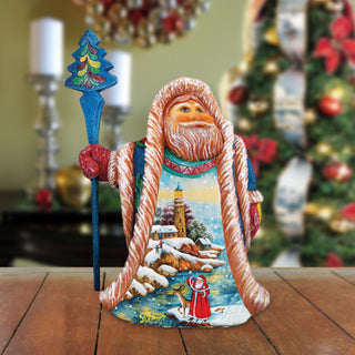 A colorful figurine of Santa Claus holding a blue staff and a wreath, with a snowy landscape and a lighthouse in the background.