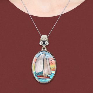 A necklace with a pendant featuring a sailboat on a body of water, with a bird in flight above the sailboat.