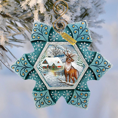 A decorative ornament featuring a deer standing in a snowy landscape, with a house and trees in the background. The ornament has a star-shaped design with intricate patterns and a gold-colored metal frame.