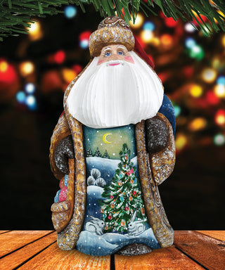 A figurine of Santa Claus with a white beard and hat, wearing a blue and gold outfit, is sitting on a wooden surface with a snowy landscape and Christmas tree in the background.
