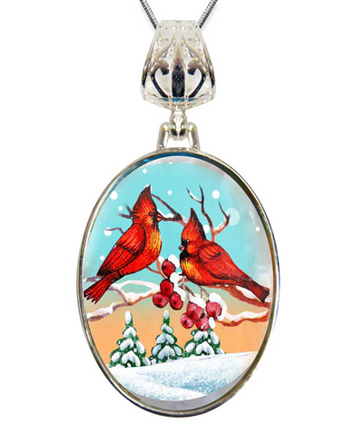 A pendant with a circular design featuring two red birds perched on branches, surrounded by snow-covered pine trees and berries.