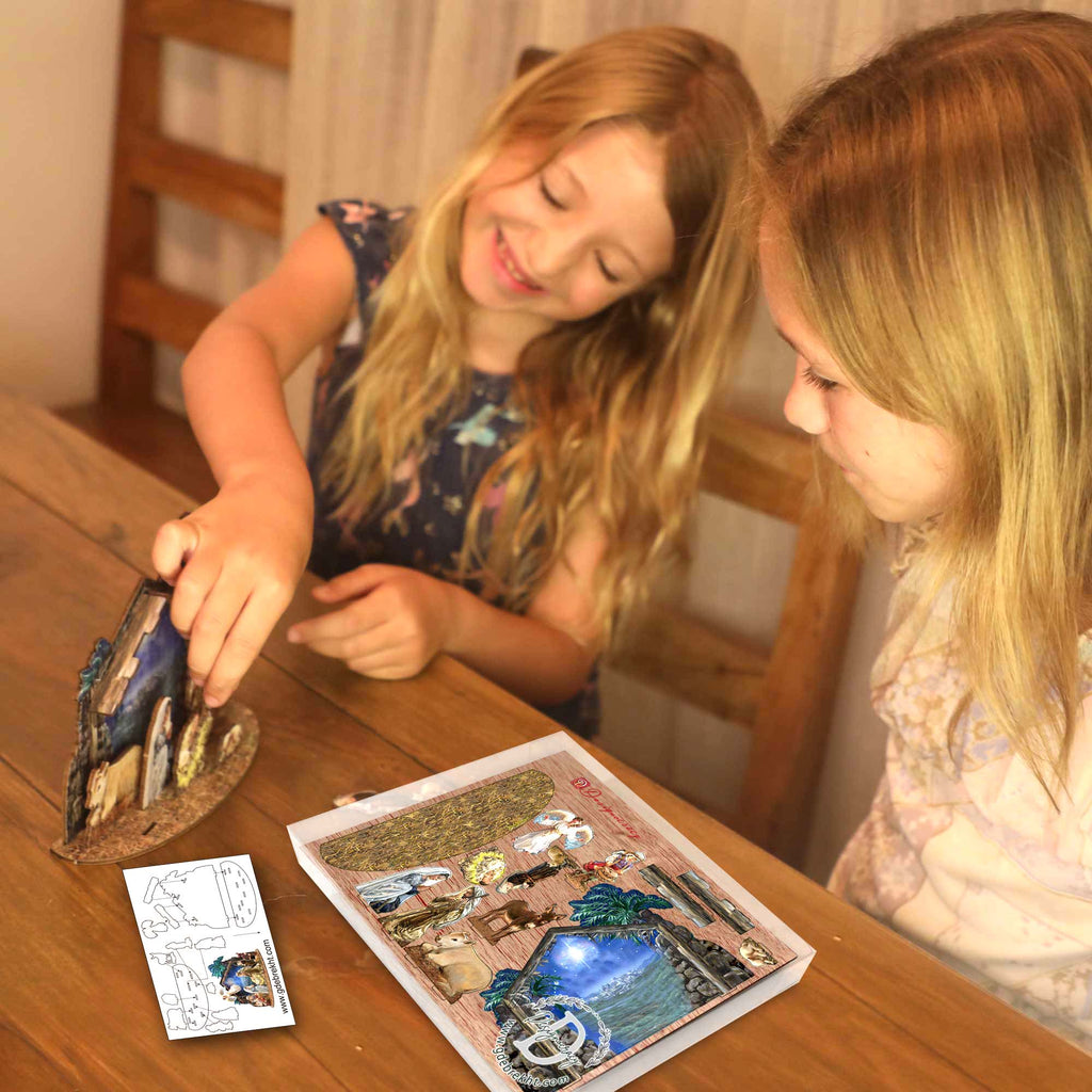 Two young girls are sitting at a table, intently focused on a craft project or activity, with a book or card in front of them.