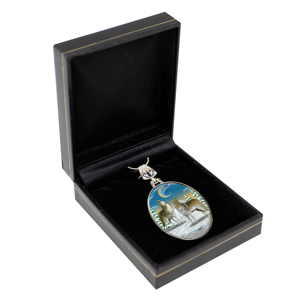 A silver pendant with a landscape scene featuring a wolf and a crescent moon, displayed in a black jewelry box.
