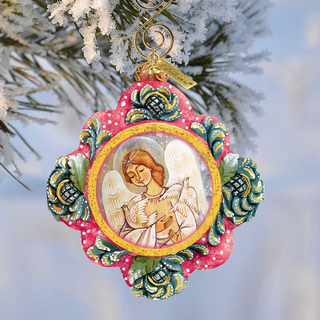 A decorative ornament featuring an angel holding a book, hanging from a tree branch with snow on the branches.