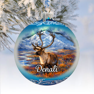 A blue ornament with a deer standing in a snowy landscape, with mountains in the background.