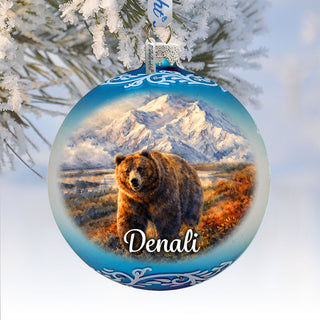 A blue ornament with a painting of a bear in front of a snowy mountain landscape.