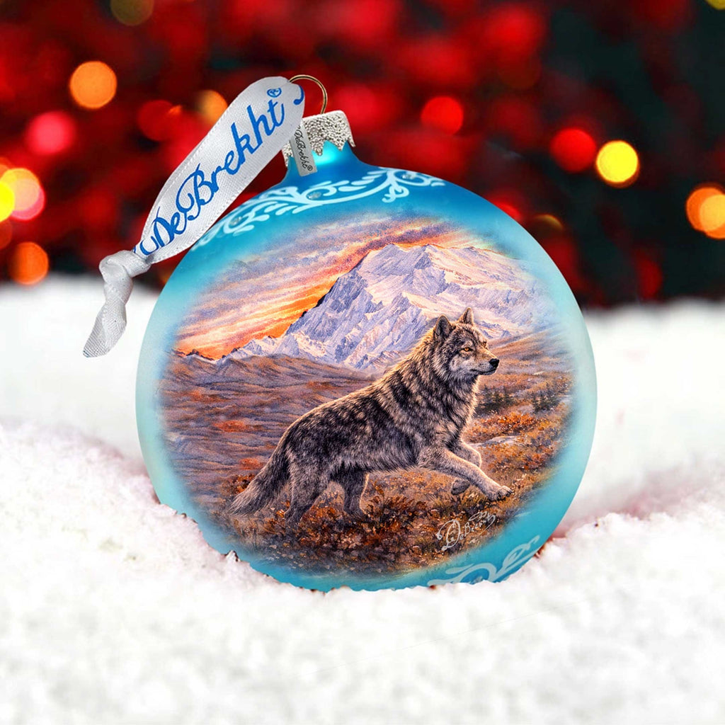 A blue ornament with a painting of a wolf in a snowy landscape, set against a background of red and orange lights.