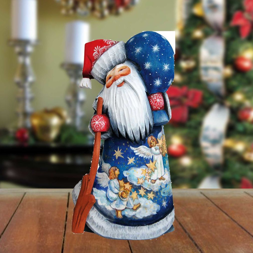 A wooden Santa Claus figurine with a blue and white color scheme, holding a broom, stands on a wooden surface.
