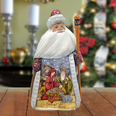 Santa Claus figurine with a nativity scene on its belly, standing on a wooden surface with a blurred background featuring a Christmas tree and other holiday decorations.