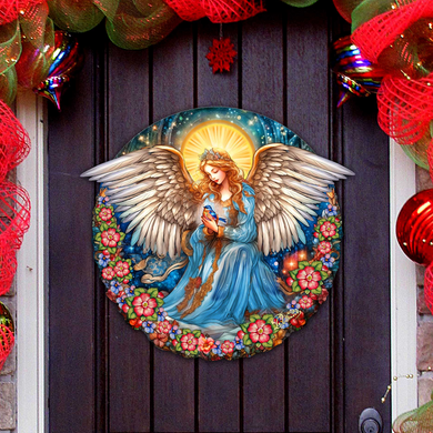 A round, painted angel figure with outstretched wings is displayed on a dark wooden door, surrounded by a colorful floral wreath and festive ornaments.