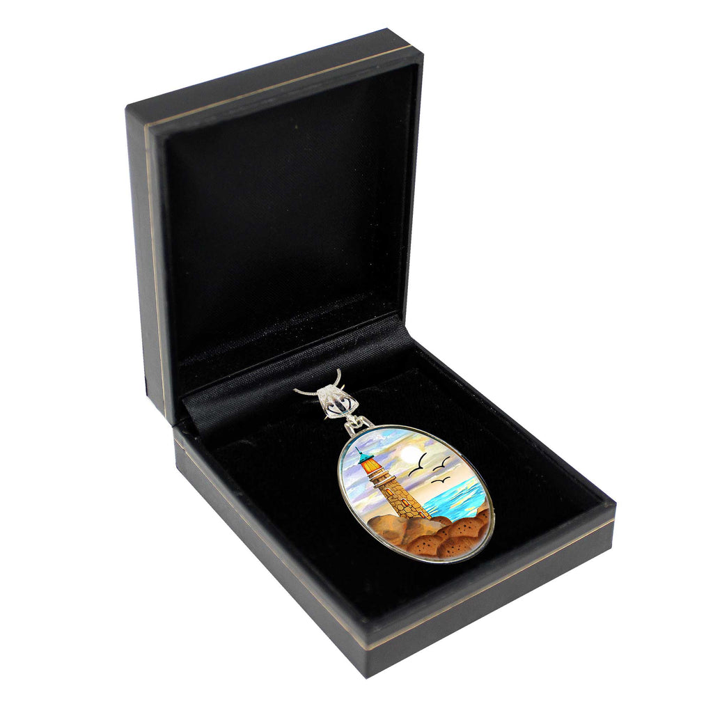A pendant with a lighthouse and a seascape design is displayed in a black jewelry box.