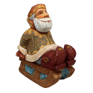 A wooden figurine of Santa Claus sitting on a sled, with intricate details and a colorful, festive appearance.