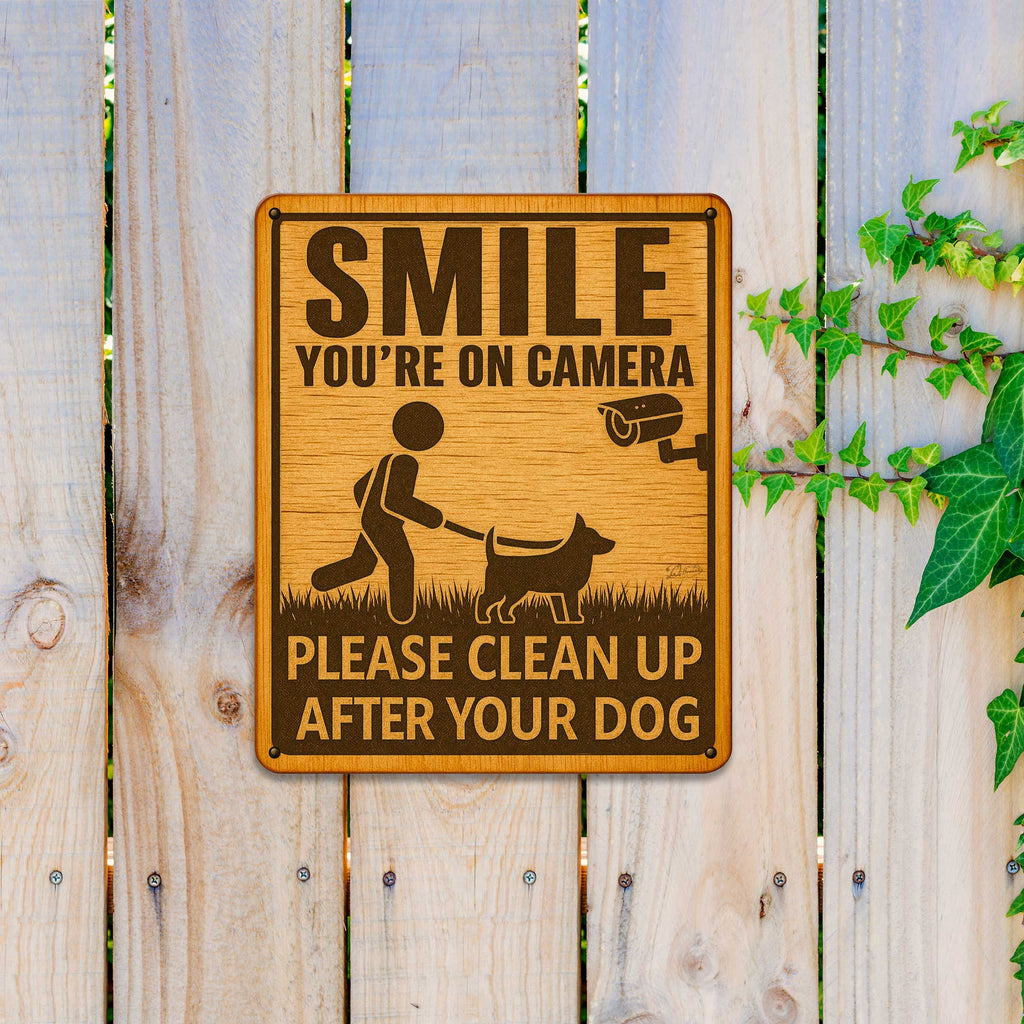 a wooden sign with a message about cleaning up after a dog, placed on a wooden fence.