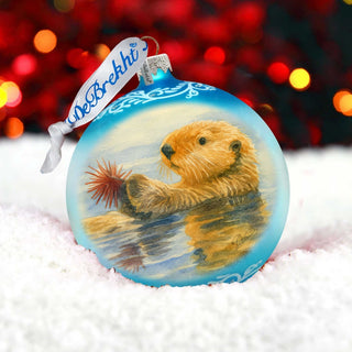 A blue ornament with a painting of an otter in the snow, set against a background of red and yellow lights.