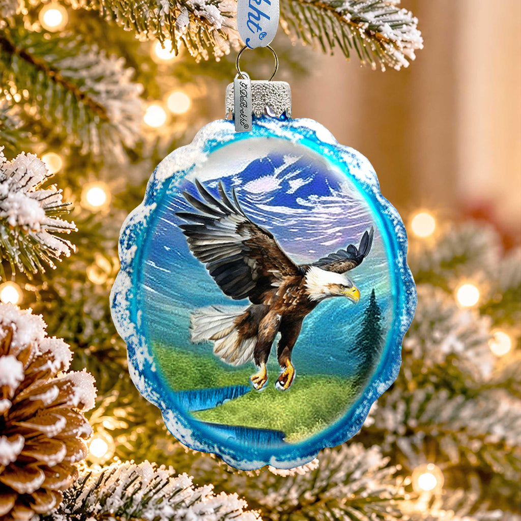 A blue ornament with a picture of a bald eagle in mid-flight, surrounded by snow-covered pine branches and twinkling lights.