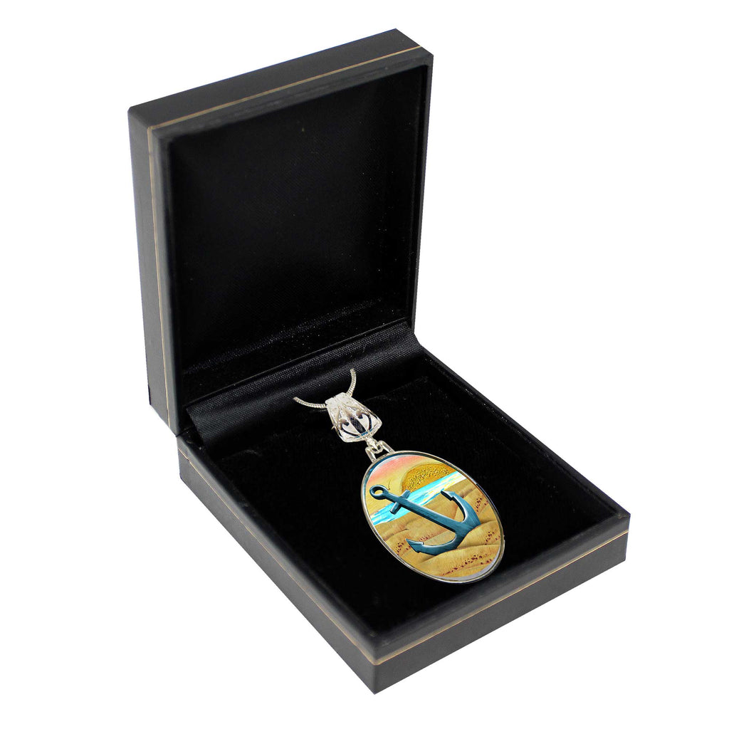 A silver necklace with a pendant featuring an anchor and a sunset in the background, displayed in a black jewelry box.