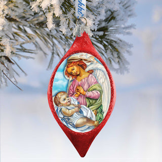 A red Christmas ornament with a painting of a baby and an angel, hanging on a tree branch covered in snow.