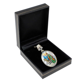 A black jewelry box containing a silver pendant with a religious scene depicted on it.