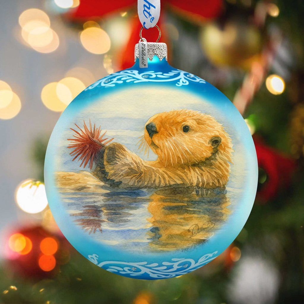 A blue ornament with a painting of an otter swimming in the water, surrounded by Christmas lights.