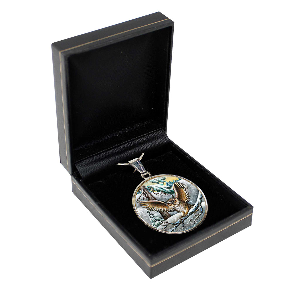 A round pendant with an eagle design is displayed in a black jewelry box.