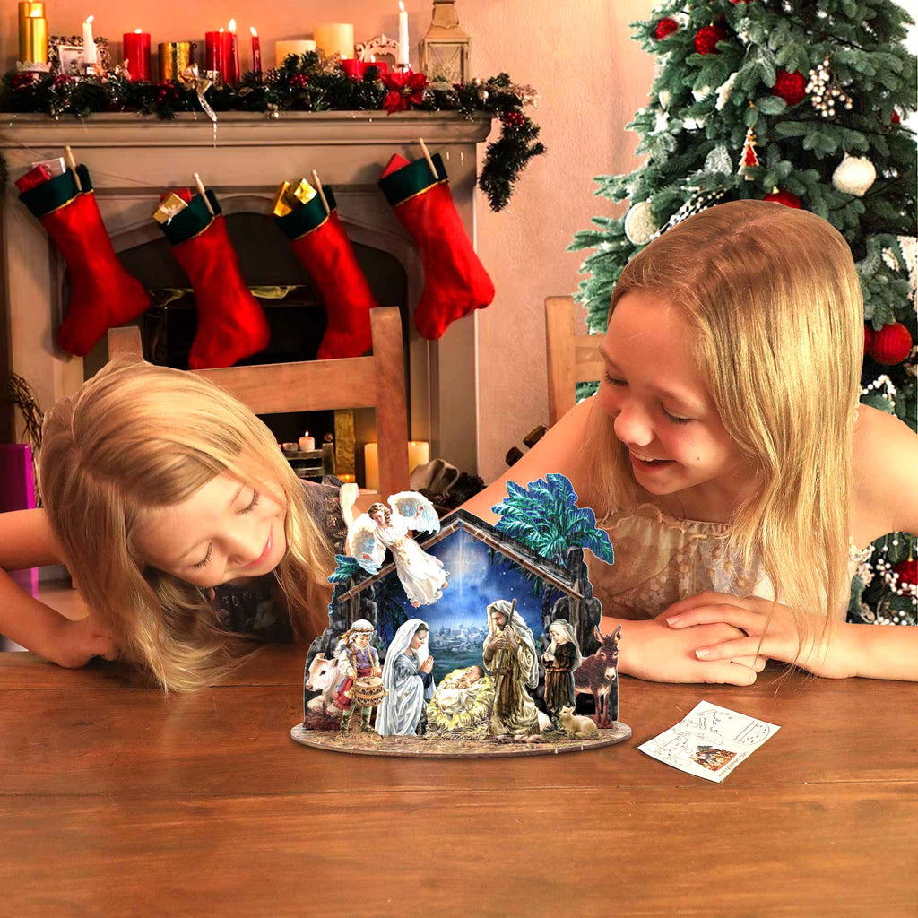 Two young girls are sitting at a table, looking at a nativity scene on a wooden table. The scene features a manger with a baby, a woman, and a child, along with other figures representing the birth of Jesus. The girls appear to be enjoying the display and are smiling at the nativity scene.