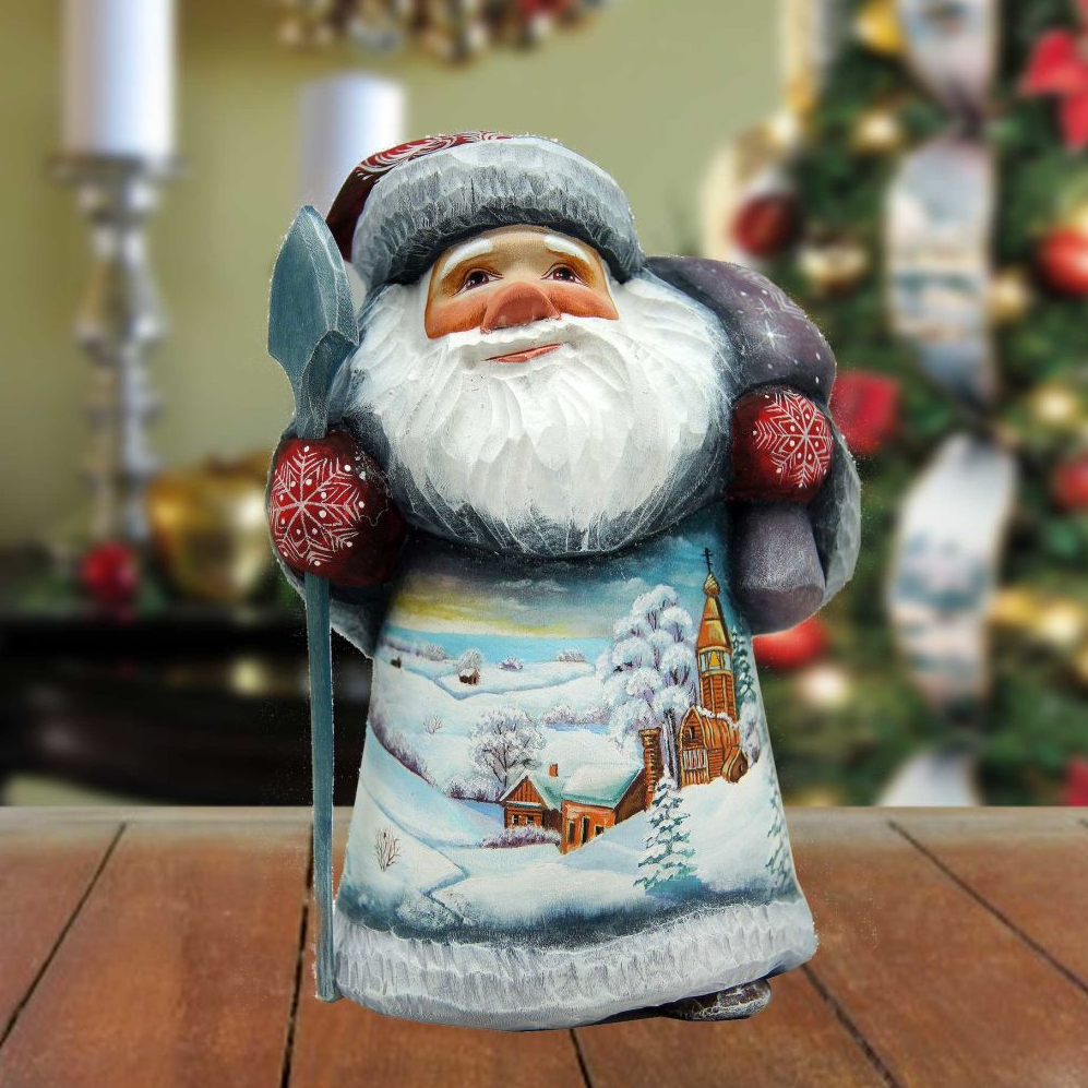A hand-painted Santa Claus figurine with a snowy landscape and a church in the background, sitting on a wooden surface.