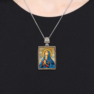 A silver necklace with a rectangular pendant featuring a religious icon, such as a saint or deity, hanging from a chain.