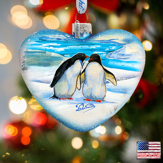 a glass ornament shaped like a heart with two penguins kissing