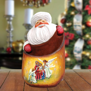 A ceramic Santa Claus figurine is displayed on a wooden surface, with a blurred Christmas tree in the background.