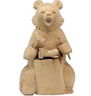 A wooden carving of a bear sitting on a wooden block, holding a small wooden object in its paws.
