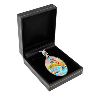 A pendant with a tropical beach scene is displayed in a black jewelry box.