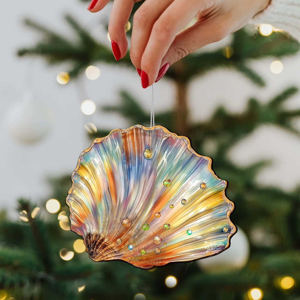 A hand holding a colorful shell ornament with a multicolored pattern, hanging from a Christmas tree.