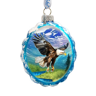 A glass ornament with a blue and white design, featuring a large eagle in flight against a mountainous landscape.