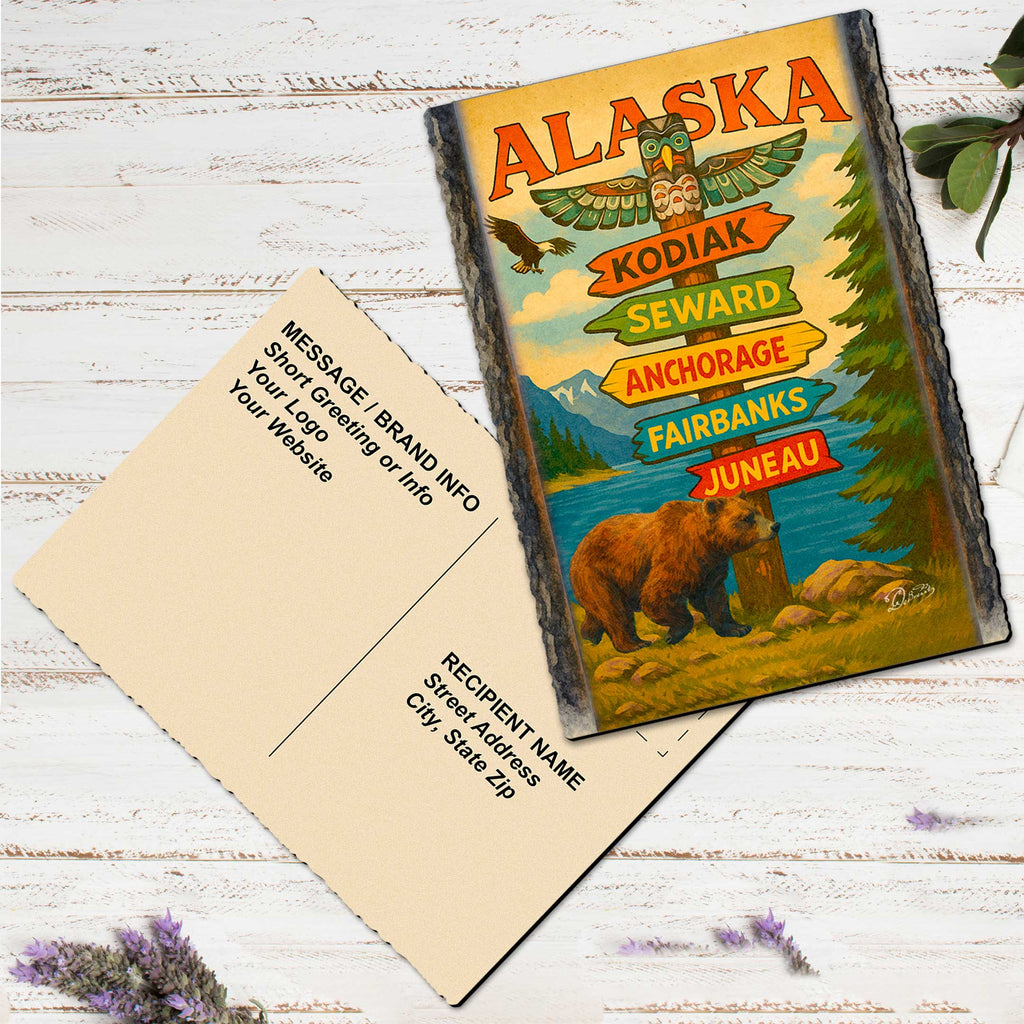 a vintage Alaska postcard with a bear illustration, placed on a white wooden surface alongside a blank white card.
