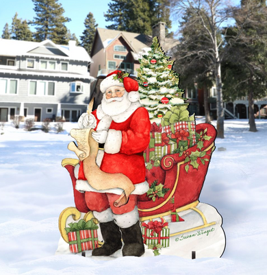 A cardboard cutout of Santa Claus sitting on a sled, surrounded by a Christmas tree and presents, with a snowy background.
