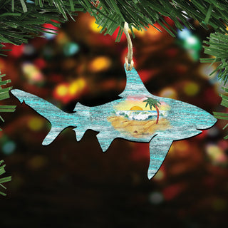 A wooden shark ornament with a beach scene inside, hanging from a branch with green leaves.