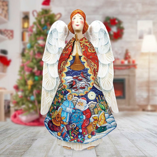 A colorful, hand-painted Christmas angel figurine stands on a wooden floor, with a blurred background featuring a decorated Christmas tree and wreath.