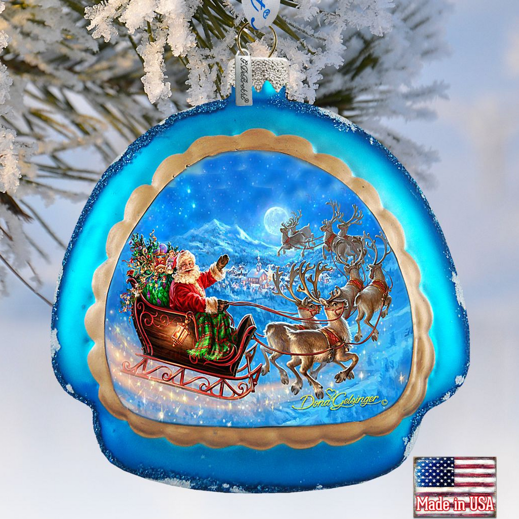 A blue ornament with a Santa Claus sleigh pulled by reindeer, set against a snowy landscape with a full moon in the night sky.