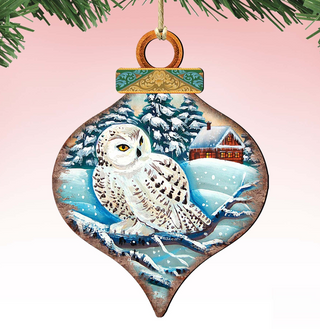 A wooden ornament in the shape of a snow owl, with a snowy landscape and a house in the background.