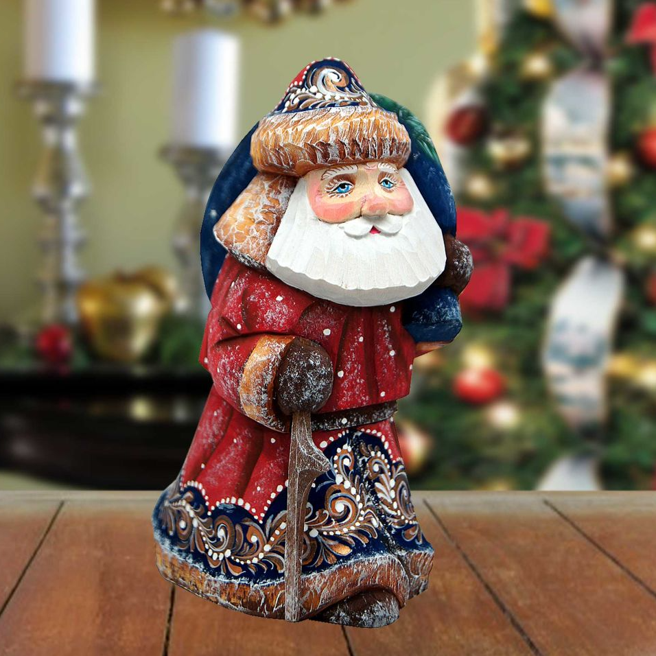 A wooden Santa Claus figurine is sitting on a wooden surface, with a blurred Christmas tree and other decorations in the background.