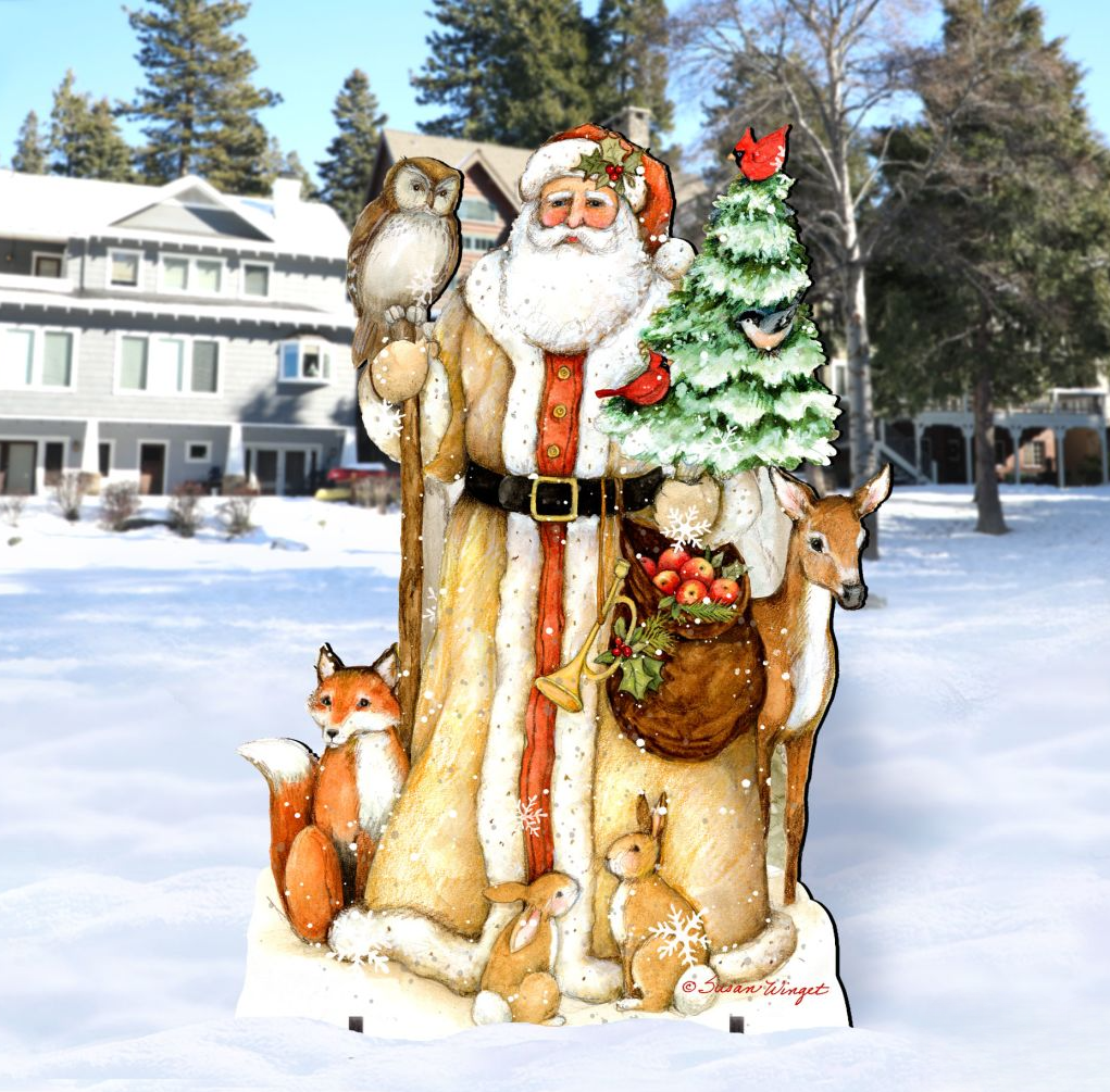 A wooden cutout of Santa Claus holding a Christmas tree, a bag of presents, and various animals such as a fox, a rabbit, and a deer, set against a snowy background with a house and trees.