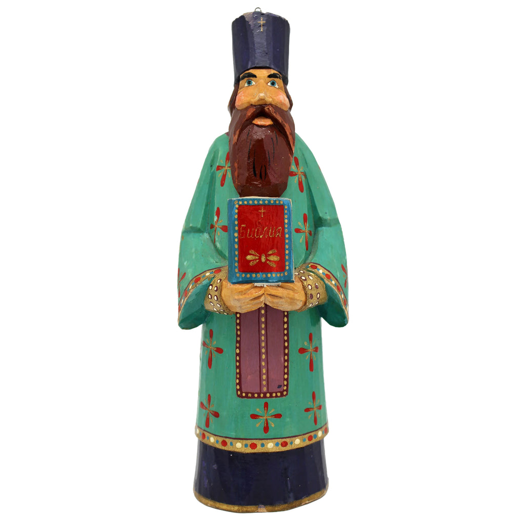 A colorful wooden statue of a bearded man wearing a green robe with red and gold accents, holding a book and standing against a white background.