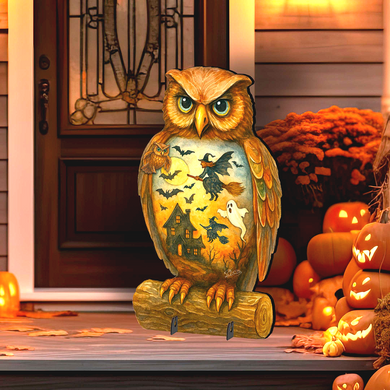 A wooden owl statue with a witch and bats on its wings stands on a wooden log, surrounded by carved pumpkins and a Halloween-themed display.
