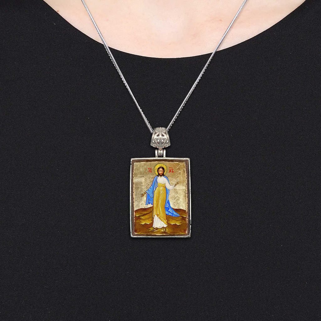 A silver necklace with a rectangular pendant featuring a religious icon.