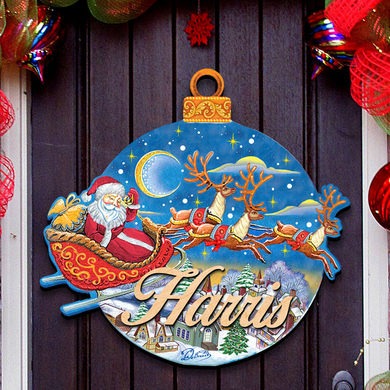 A decorative Christmas ornament hanging on a door, featuring a Santa Claus sleigh in motion and reindeer flying in the background.