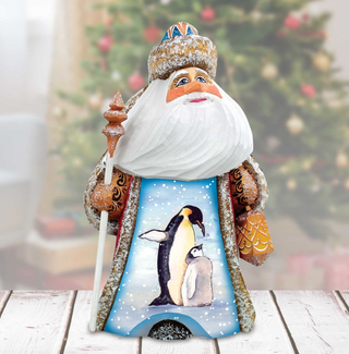 A wooden Santa Claus figurine with a penguin design on its chest, standing on a wooden surface.
