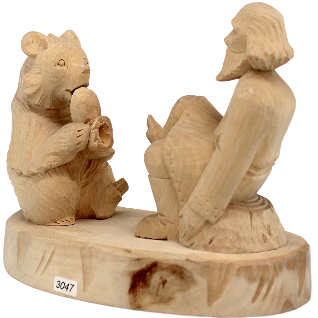 A wooden sculpture depicting a bear sitting on a rock and playing a musical instrument, with a carved human figure seated next to it.