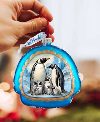 a hand holding a christmas ornament with penguins on it